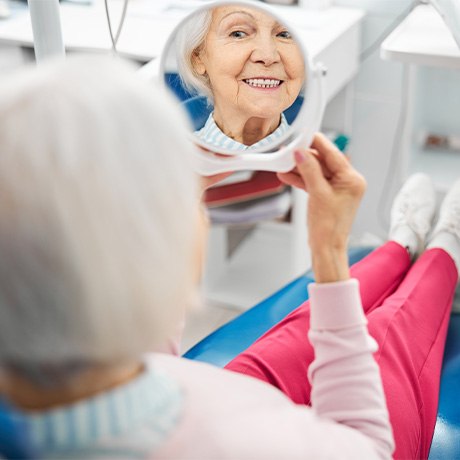 Senior dental patient holding hand mirror, looking at her teeth