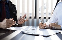 Two people sitting at desk, discussing paperwork